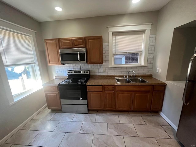 kitchen featuring brown cabinetry, decorative backsplash, stainless steel appliances, and a sink