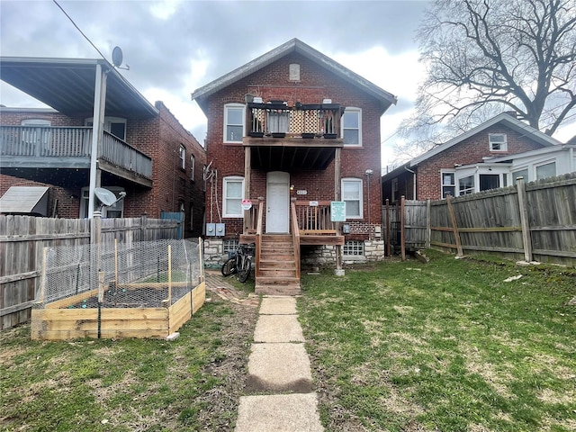 rear view of property with brick siding, a fenced backyard, a yard, a balcony, and a vegetable garden