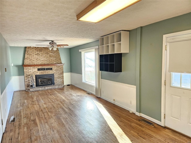 unfurnished living room featuring visible vents, wood finished floors, a wainscoted wall, and ceiling fan