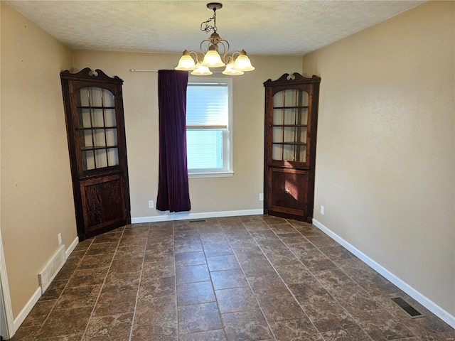 unfurnished dining area featuring a chandelier, visible vents, a textured ceiling, and baseboards