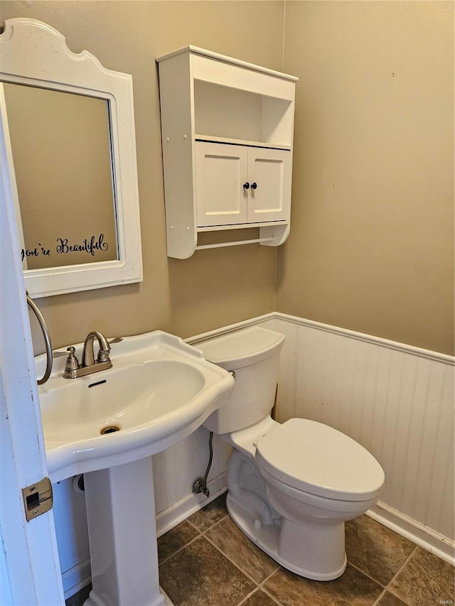 half bathroom with wainscoting, toilet, and a sink