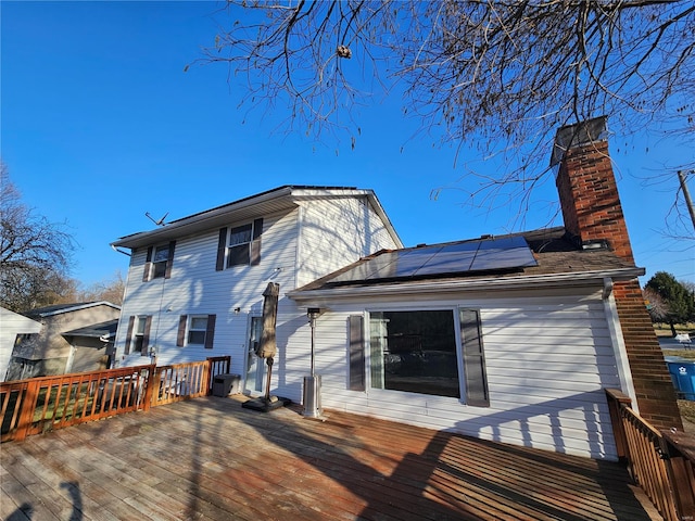 back of house featuring a wooden deck, roof mounted solar panels, and a chimney