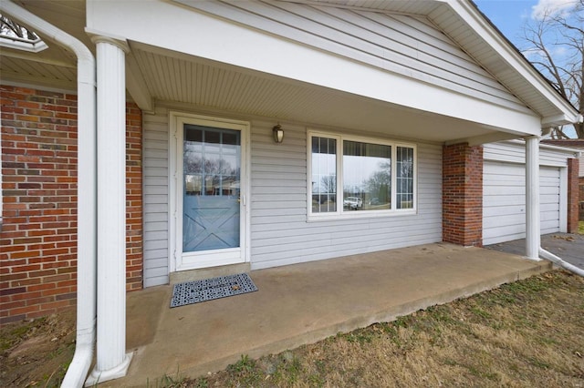 entrance to property featuring a porch, a garage, and brick siding