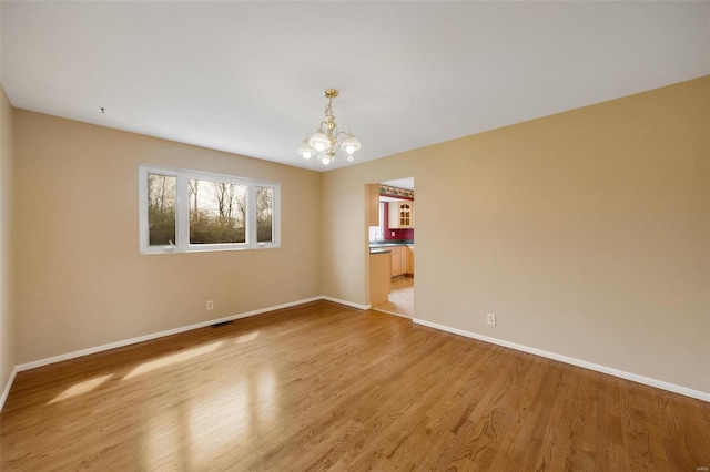 spare room featuring baseboards, light wood-style floors, and an inviting chandelier