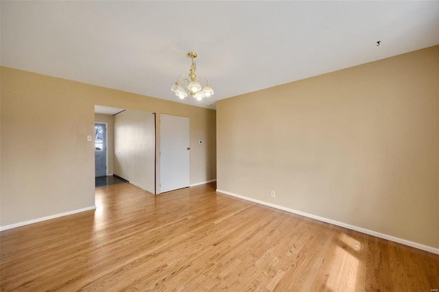 spare room featuring a notable chandelier, light wood-style flooring, and baseboards