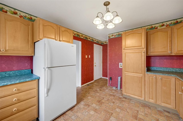 kitchen featuring dark countertops, brick floor, freestanding refrigerator, and a chandelier