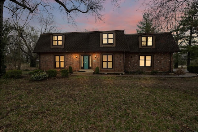 view of front of property with brick siding, mansard roof, a shingled roof, and a yard