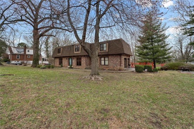 colonial inspired home with brick siding, mansard roof, a shingled roof, and a front yard