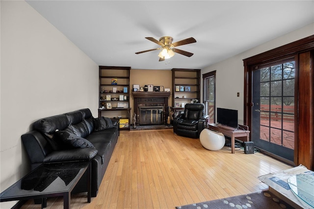 living area featuring a glass covered fireplace, ceiling fan, and light wood-style floors