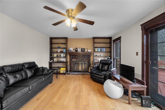 living room with a glass covered fireplace, light wood-style flooring, and a ceiling fan