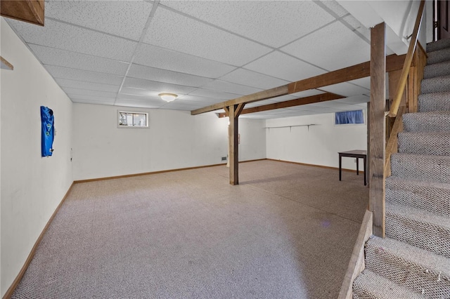 basement featuring a drop ceiling, stairway, and baseboards