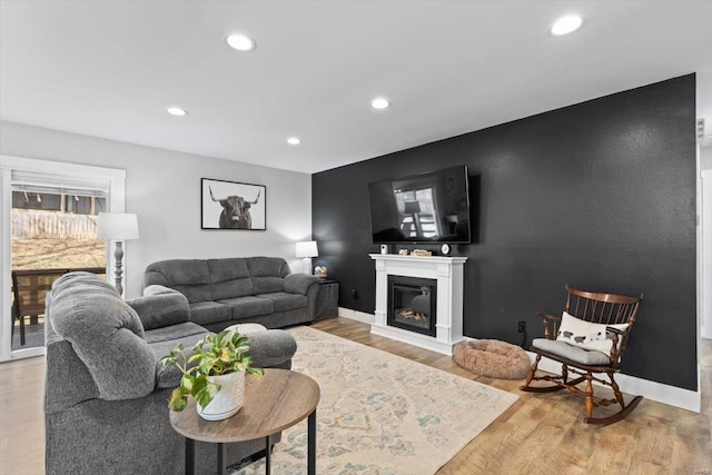 living room with an accent wall, baseboards, recessed lighting, wood finished floors, and a glass covered fireplace