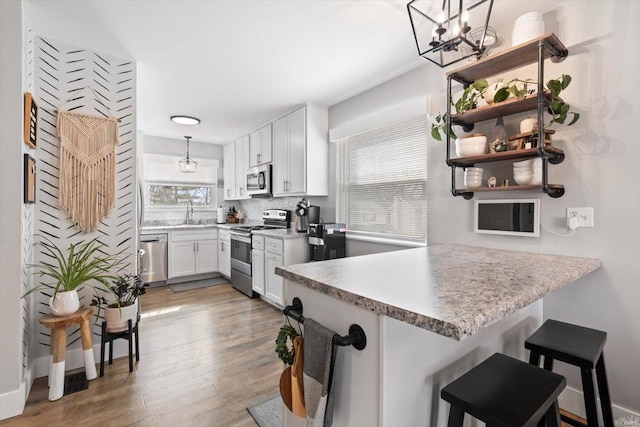 kitchen with backsplash, wood finished floors, stainless steel appliances, a peninsula, and white cabinets