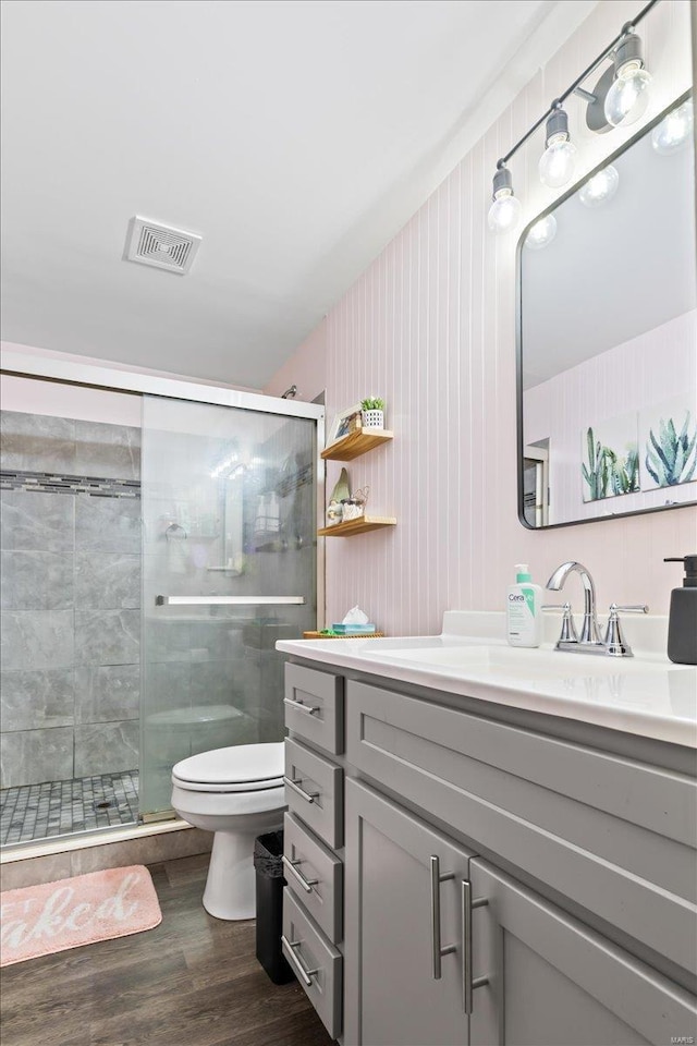 bathroom featuring visible vents, a shower stall, toilet, wood finished floors, and vanity