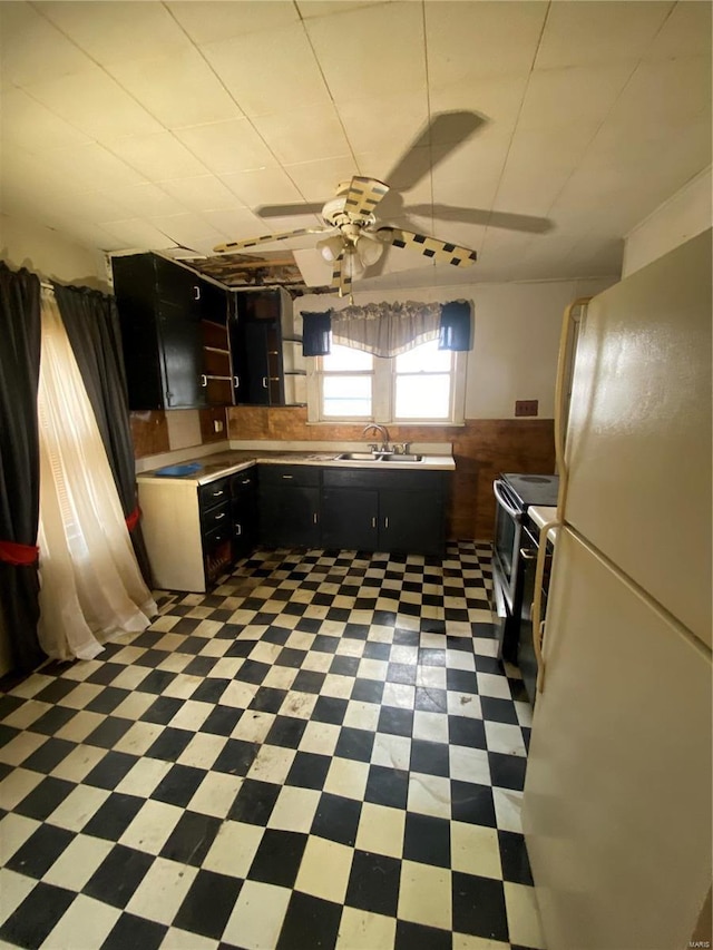 kitchen featuring dark cabinetry, light floors, freestanding refrigerator, stainless steel range with electric cooktop, and a sink