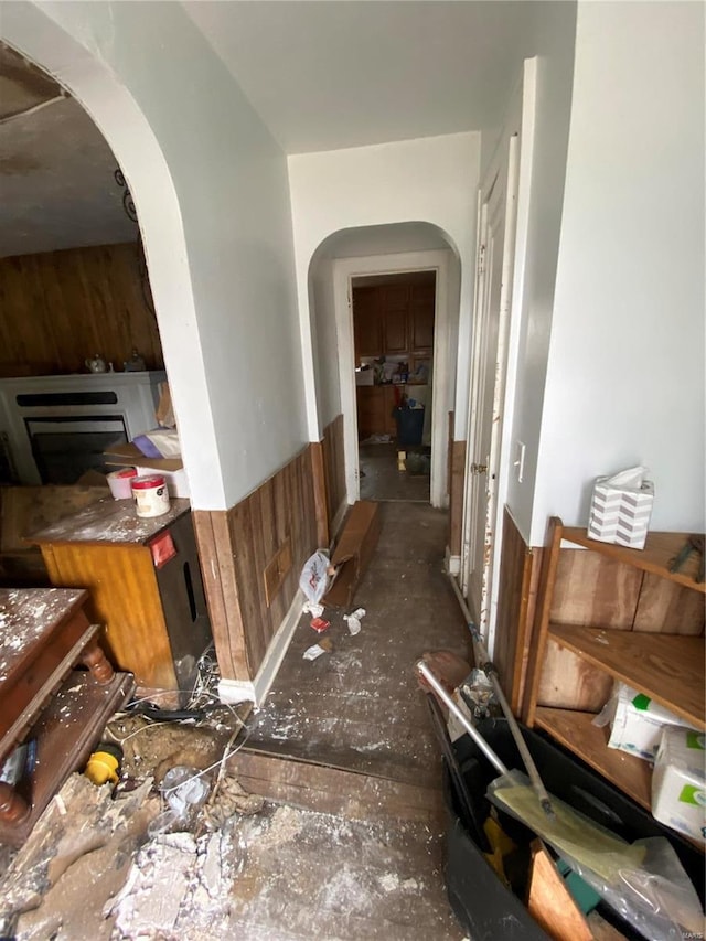 hall featuring wooden walls, arched walkways, and wainscoting