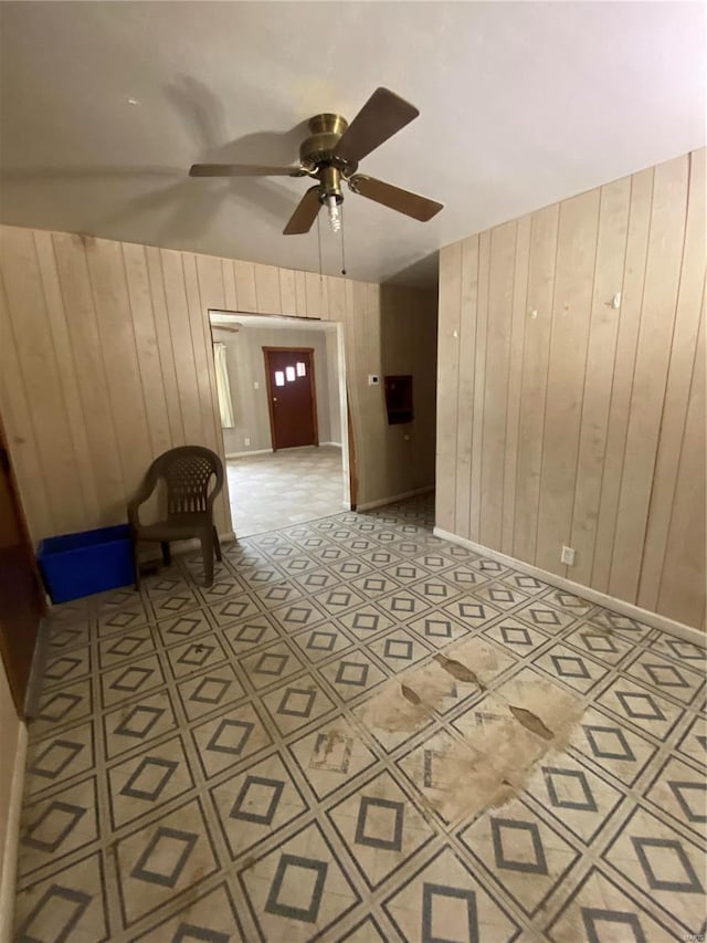 empty room featuring wooden walls, baseboards, and a ceiling fan