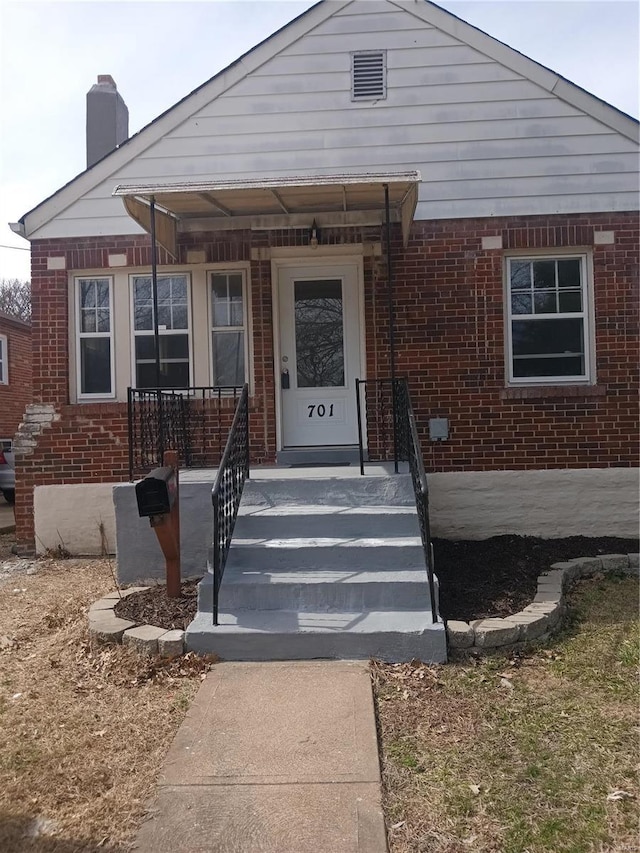 bungalow-style home with a porch, brick siding, and a chimney