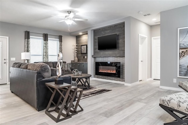 living area with visible vents, light wood-style flooring, a ceiling fan, a large fireplace, and baseboards