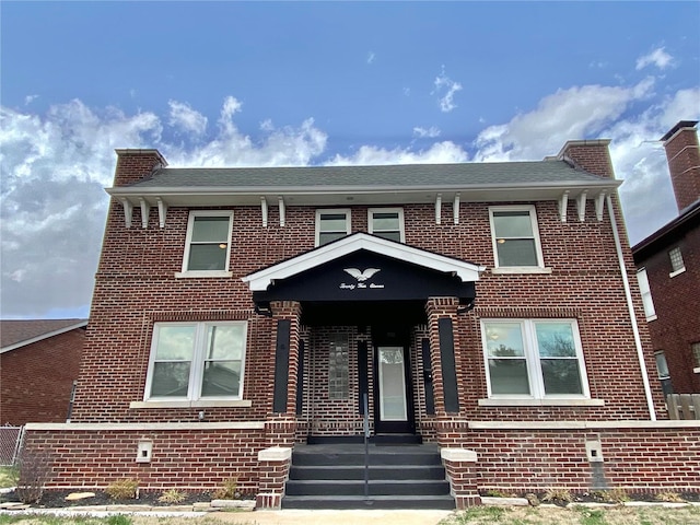 view of front facade with brick siding and roof with shingles