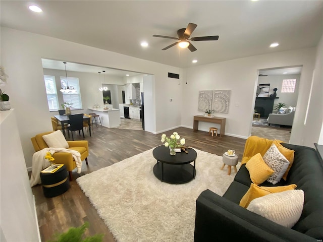 living area featuring recessed lighting, dark wood-type flooring, and ceiling fan with notable chandelier