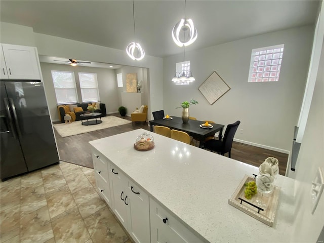 kitchen with light stone counters, white cabinetry, ceiling fan, black refrigerator with ice dispenser, and hanging light fixtures