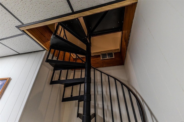 stairway with visible vents and a drop ceiling