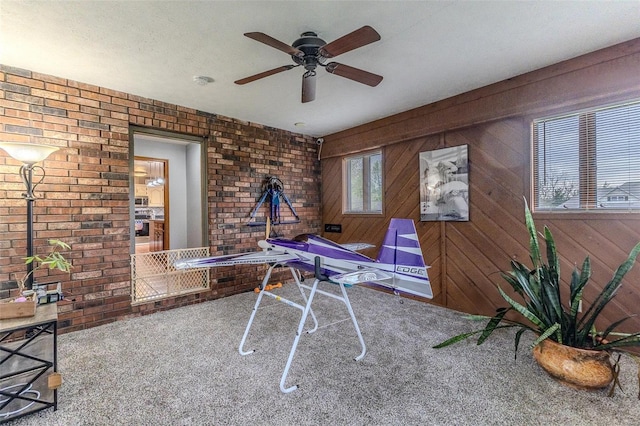 unfurnished office featuring wood walls, brick wall, ceiling fan, and carpet