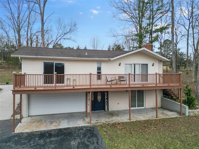 rear view of house featuring a patio, driveway, an attached garage, a chimney, and a deck