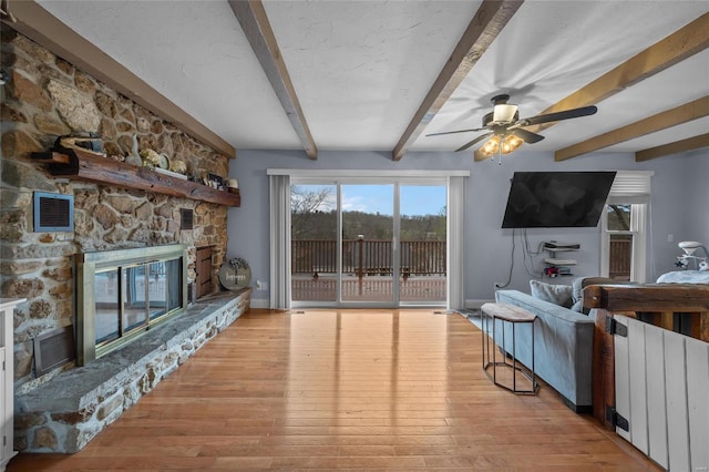 living area with visible vents, beam ceiling, a stone fireplace, light wood finished floors, and ceiling fan