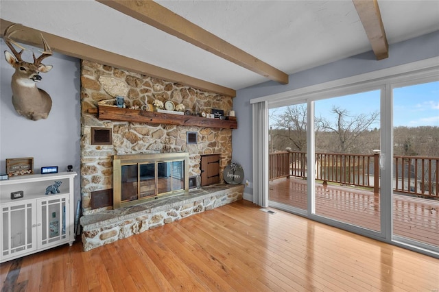 living room with beam ceiling, visible vents, a fireplace, and hardwood / wood-style floors