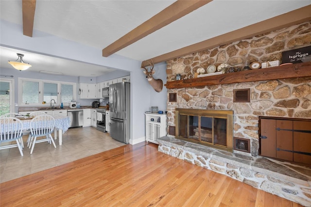 living room with visible vents, beamed ceiling, a fireplace, and light wood-style flooring