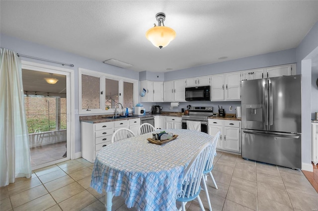 kitchen with a sink, stainless steel appliances, light tile patterned floors, and white cabinetry