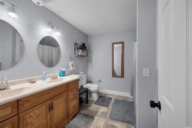 bathroom with a sink, toilet, double vanity, and a textured ceiling