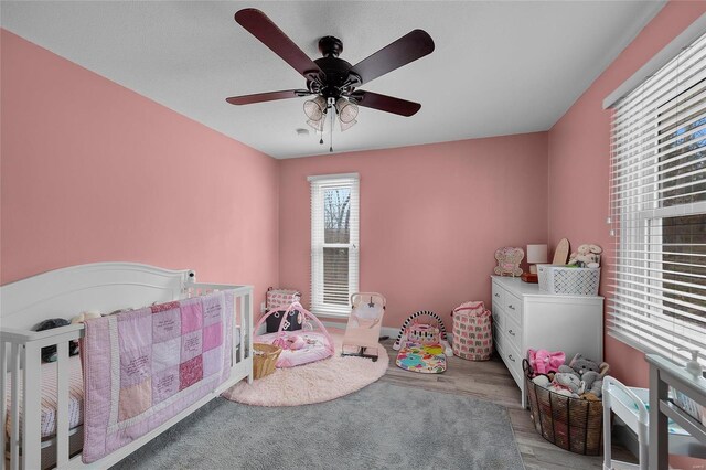 bedroom with ceiling fan, a nursery area, and wood finished floors