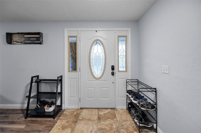 foyer entrance with stone finish flooring, baseboards, a textured ceiling, and a textured wall