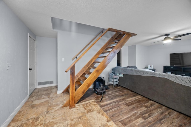 living area featuring visible vents, ceiling fan, stairs, wood finished floors, and a textured ceiling