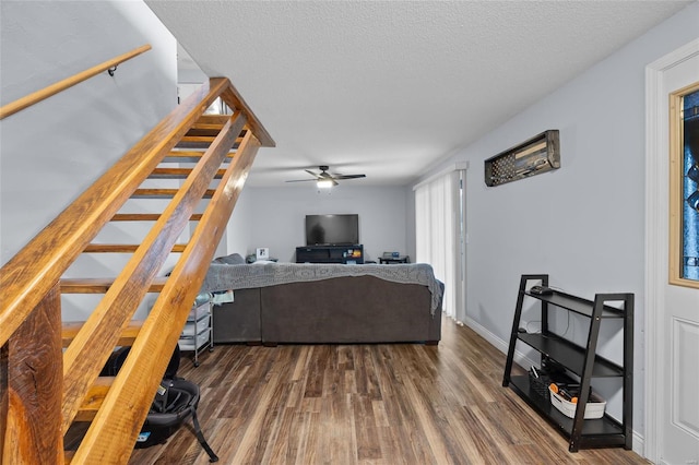 living area with stairway, a ceiling fan, baseboards, dark wood-type flooring, and a textured ceiling