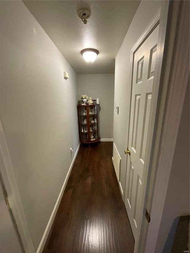 hallway with baseboards, a textured ceiling, and dark wood-style flooring