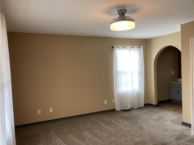 spare room with arched walkways, baseboards, and carpet