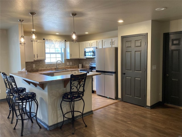 kitchen with a kitchen bar, a peninsula, white cabinets, stainless steel appliances, and a sink