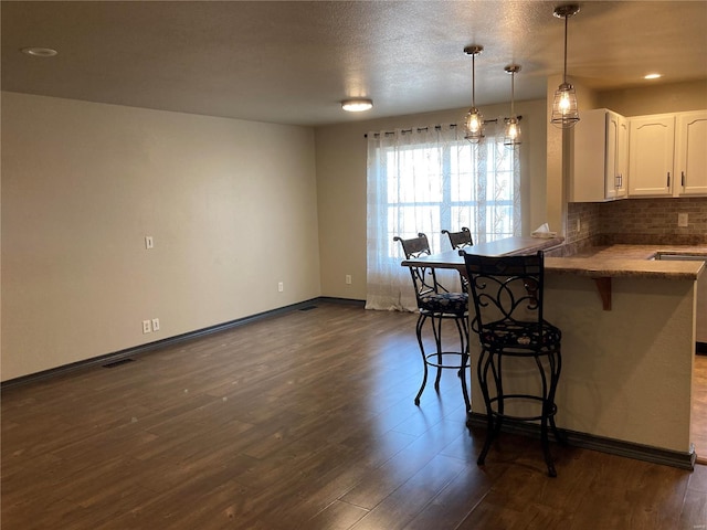 kitchen with tasteful backsplash, white cabinets, a kitchen breakfast bar, and dark wood-style flooring