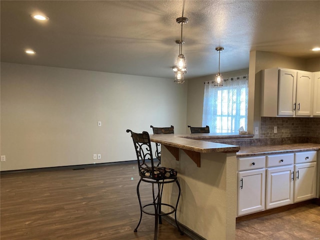 kitchen featuring dark wood finished floors, a breakfast bar, white cabinets, dark countertops, and backsplash