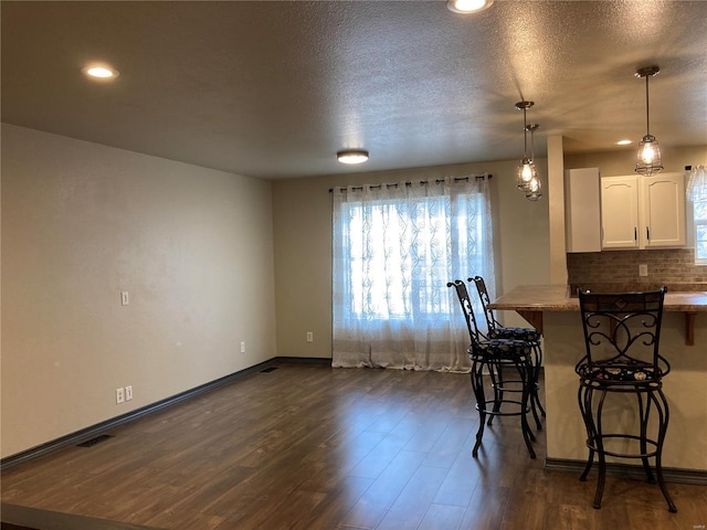 kitchen with a breakfast bar area, decorative backsplash, dark wood-type flooring, hanging light fixtures, and white cabinets