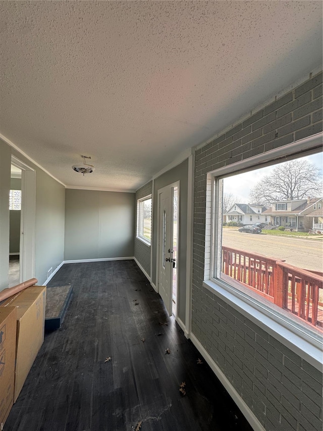 interior space with baseboards, a textured ceiling, brick wall, and wood finished floors