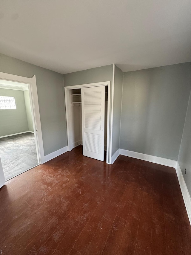 unfurnished bedroom with baseboards, a closet, and dark wood-type flooring