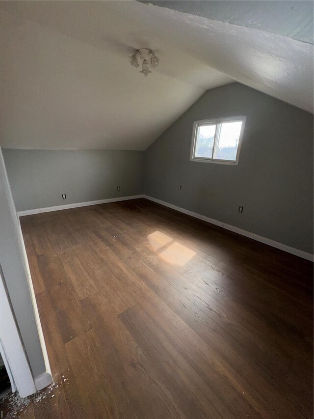 additional living space featuring dark wood-type flooring, baseboards, and vaulted ceiling