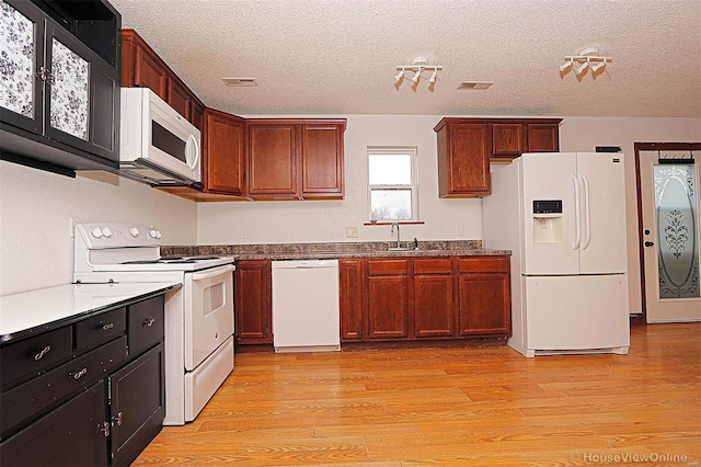 kitchen featuring visible vents, a sink, a textured ceiling, white appliances, and light wood finished floors