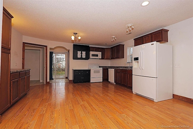 kitchen with white appliances, arched walkways, a sink, light wood-style floors, and a textured ceiling