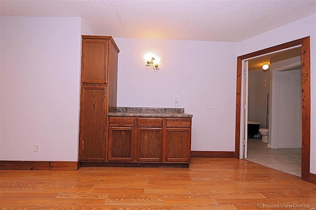 interior space featuring light wood finished floors, dark countertops, baseboards, brown cabinets, and a textured ceiling